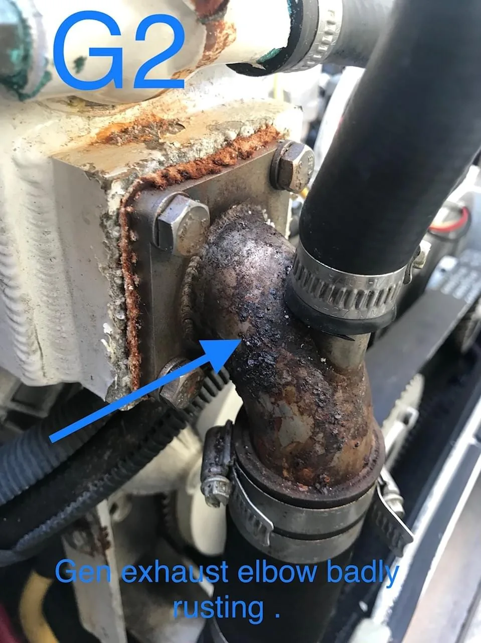 Survey finding photograph marked G2 showing a badly rusting generator exhaust elbow with blue callout arrows
