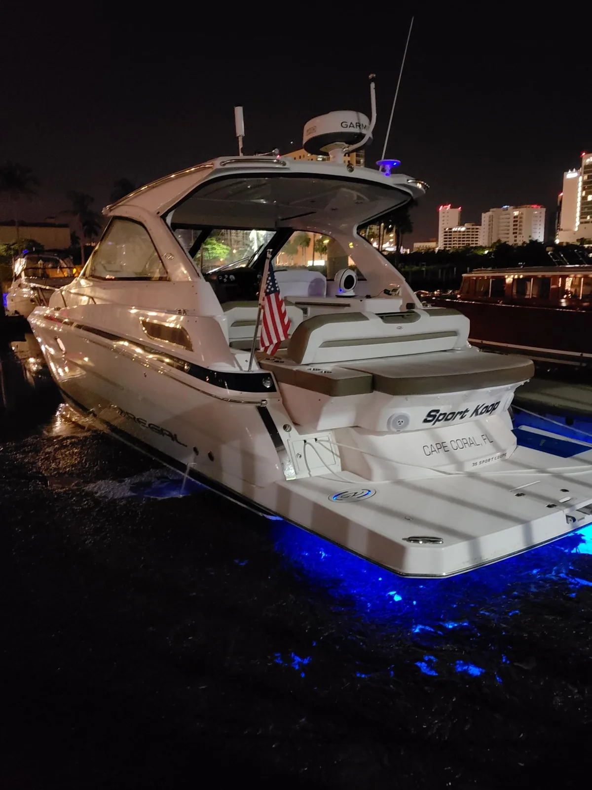 Motor yacht lit at a dock at night with underwater lights on